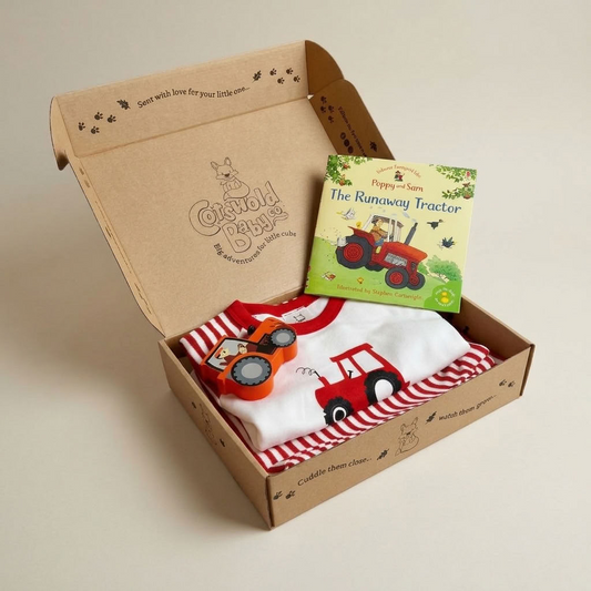 A baby gift set in a branded cardboard box, featuring a white and red striped long-sleeve shirt with a red tractor graphic, a red toy tractor, and a children's book titled 'The Runaway Tractor' by Pippi and Barn.