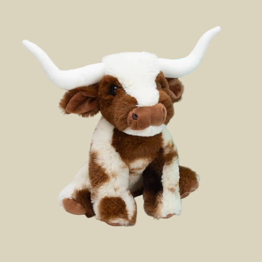 A small plush toy resembling a Texas Longhorn cow with a white body and brown accents, sitting beside a turquoise bag with a bull graphic on it.