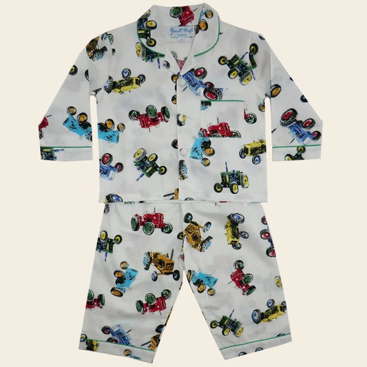 A two-piece children's pajama set featuring a white long-sleeve top and matching pants, both printed with a colorful pattern of cartoon tractors and farm vehicles.