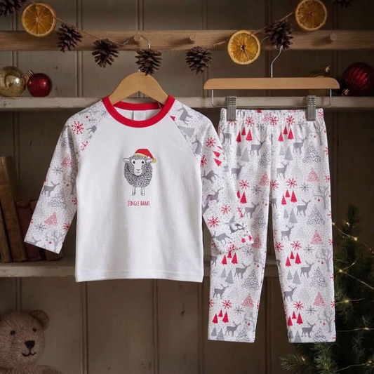 A two-piece children's pajama set hanging on wooden hangers against a rustic holiday shelf backdrop. The set includes a white long-sleeve top with red raglan sleeves and collar, featuring a sheep wearing a Santa hat and the text 'JINGLE BELL', and matching white pants with a red and gray Christmas tree and reindeer pattern.