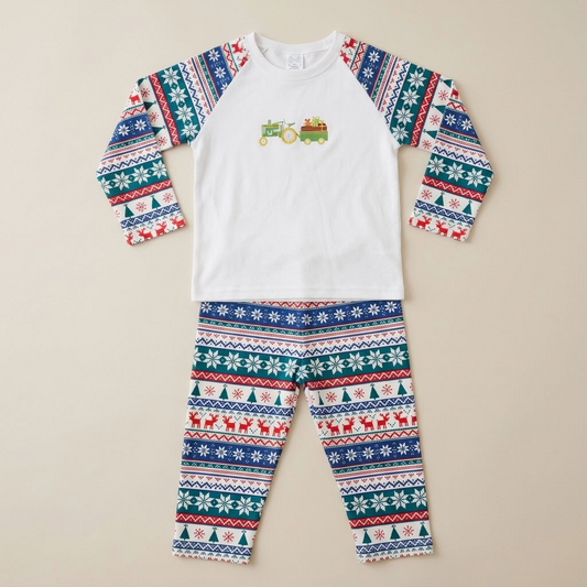 A two-piece children's pajama set laid flat on a light beige background. The long-sleeve top is white with a small green tractor graphic on the chest and features a festive Fair Isle pattern on the sleeves in blue, green, red, and white.