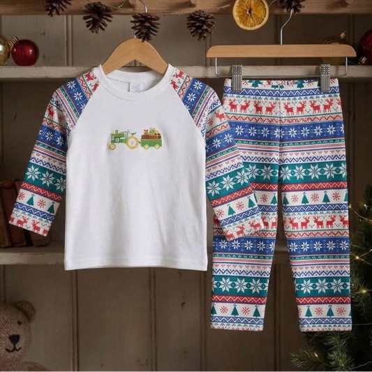 A children's holiday pajama set hanging on wooden hangers, featuring a white long-sleeve top with multicolor Fair Isle patterned raglan sleeves and a small tractor graphic on the chest, paired with matching patterned pants.