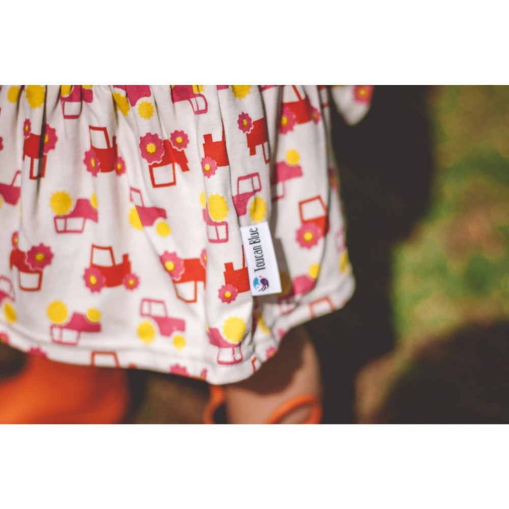 little girl in woods wearing red short sleeve tractor dress from toucan blue | Cotswold Baby Co