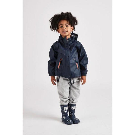 Little boy wearing a navy waterproof rain cheater coat by grass and air, Cotswold Baby Co