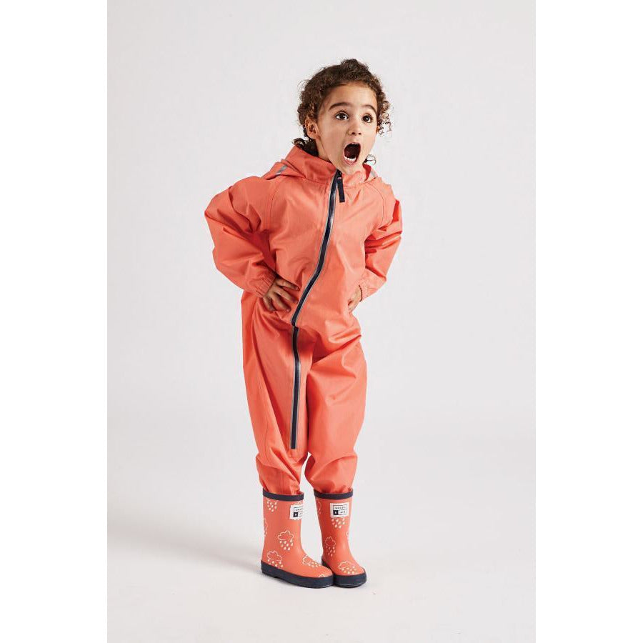 Little girl wearing coral stomper suit by grass and air - Cotswold Baby Co
