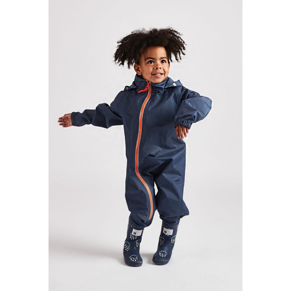 Little boy wearing navy waterproof stomper suit by grass and air - Cotswold Baby Co