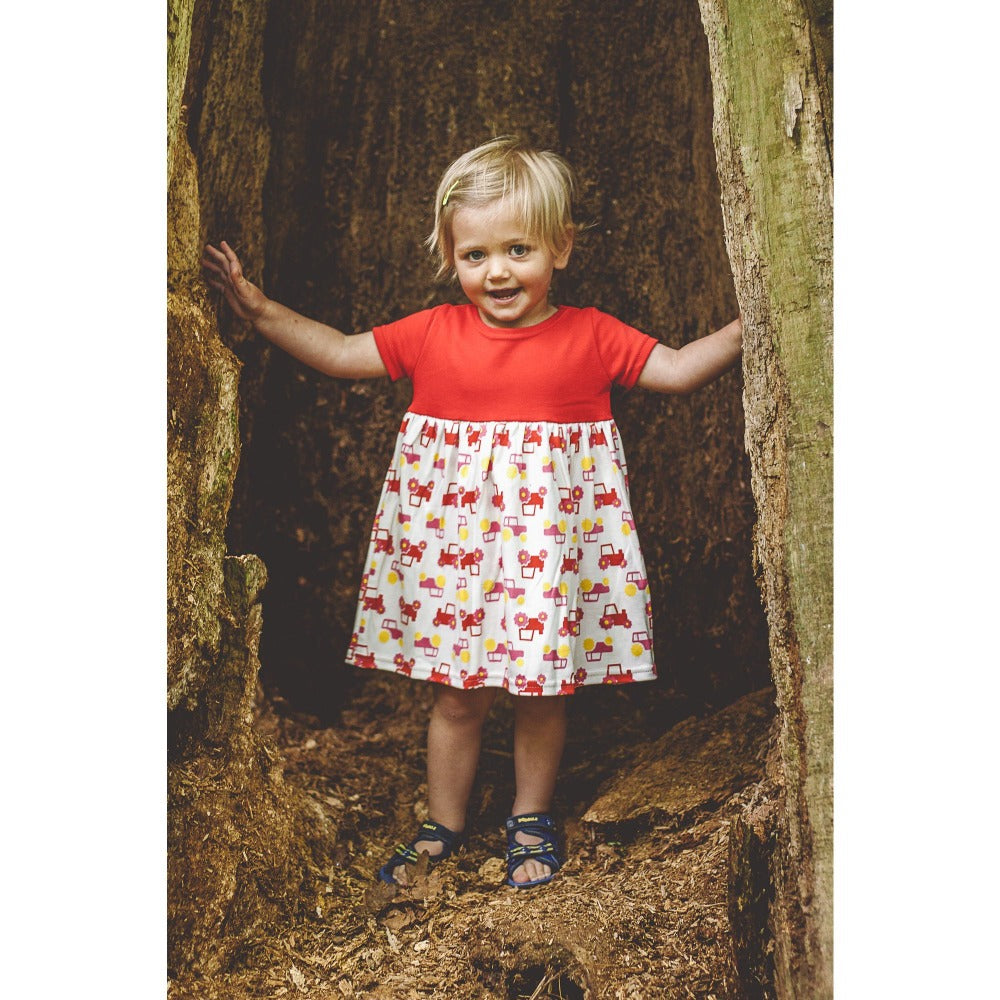 little girl in woods wearing red short sleeve tractor dress from toucan blue | Cotswold Baby Co