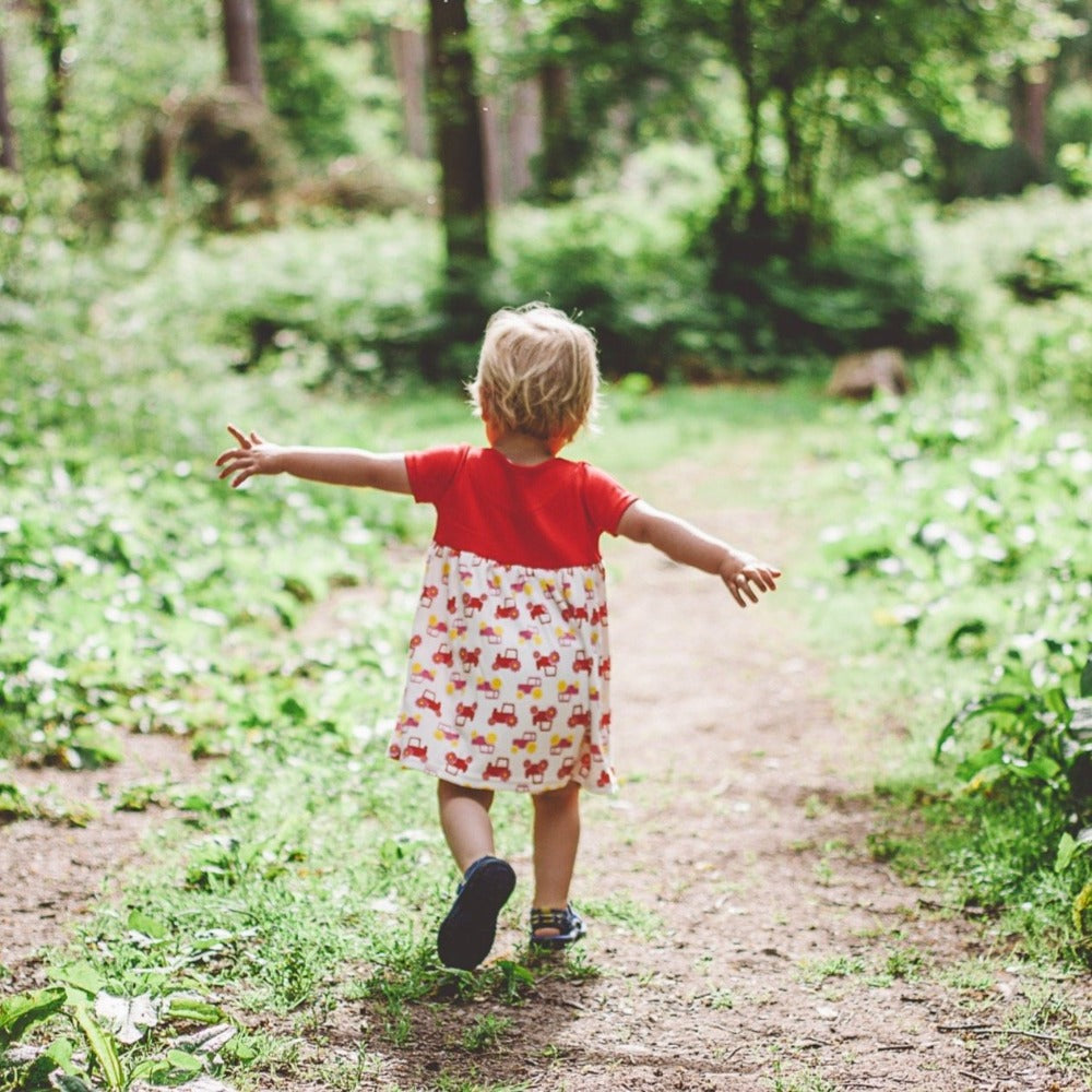 little girl in woods wearing red short sleeve tractor dress from toucan blue | Cotswold Baby Co